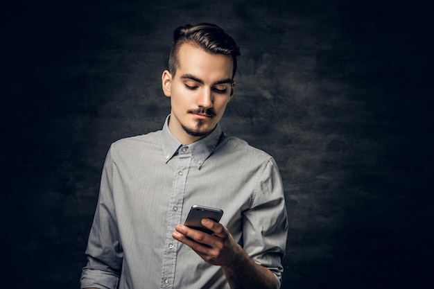 Studio portrait of handsome bearded hipster male with a tattoo on his arm using a smartphone.