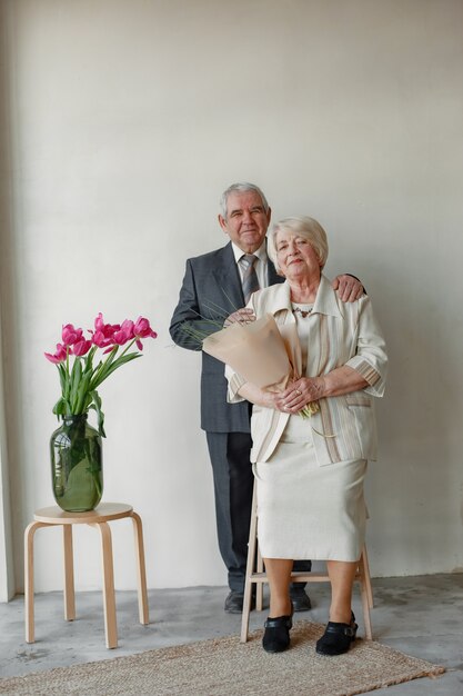 灰色の壁に抱きしめる幸せな老夫婦のスタジオポートレート。