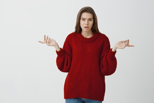 Ritratto in studio di intensa donna europea arrabbiata in maglione sciolto alla moda, che punta lateralmente con la faccia scontenta, essere infastidita e arrabbiata durante il litigio