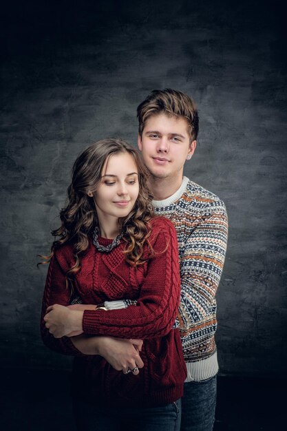 Studio portrait of loving couple in winter warm pullovers on grey background.