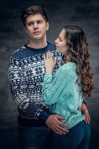 Студийный портрет любящей пары в зимних теплых пуловерах на сером фоне.