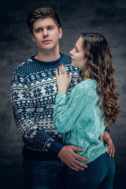 회색 바탕에 따뜻한 겨울 스웨터를 입은 사랑스러운 부부의 스튜디오 초상화.