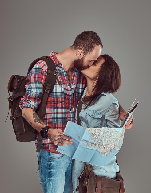 Студийный портрет мужчин и женщин-туристов с рюкзаком и картой, обнимающихся в студии. Изолированные на сером фоне.