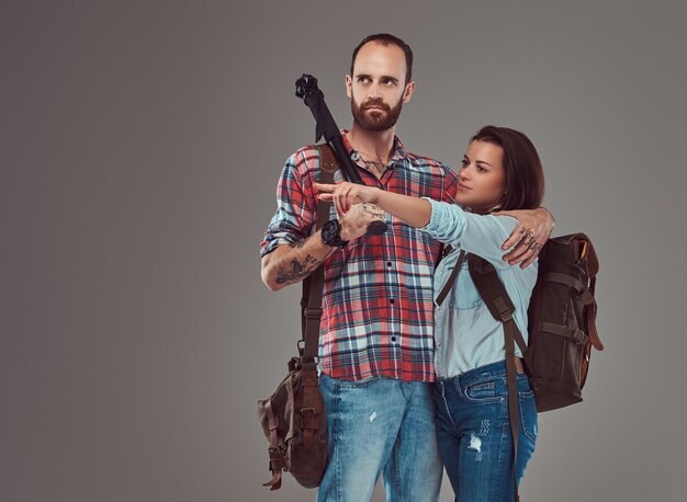 Studio portrait of male and female tourists with backpack and tripod, cuddling in a studio. Isolated on a gray background.