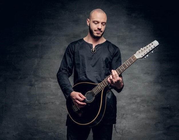 Studio portrait of a man in traditional Celtic clothes playing on mandolin over grey vignette background.