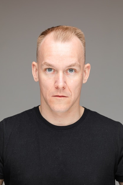 Бесплатное фото Студийный портрет взрослого белокурого человека кавказа с короткой стрижкой в черной футболке с голубыми глазами, глядя в камеру на сером фоне.