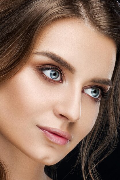 Studio portrait of perfect brunette with professional makeup and hairstyle from beauty salon wearing diamond earring over black background