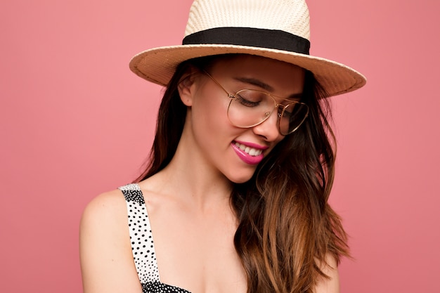 Studio portrait of pleased beautiful female posing in spectacles and summer hat