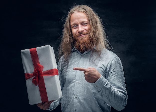 Foto gratuita il ritratto in studio di un uomo barbuto positivo con i capelli lunghi tiene la scatola attuale.