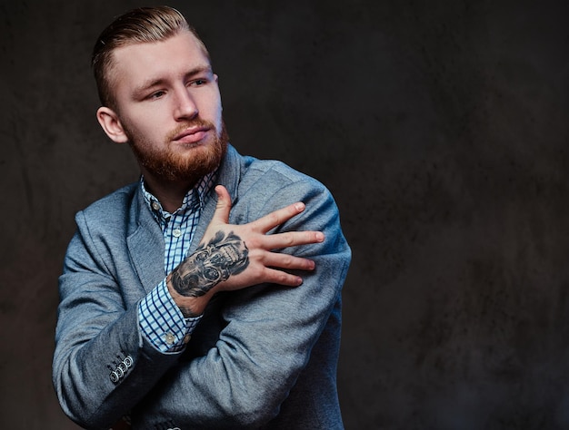 Studio portrait of redhead bearded male dressed in a suit posing over grey background.