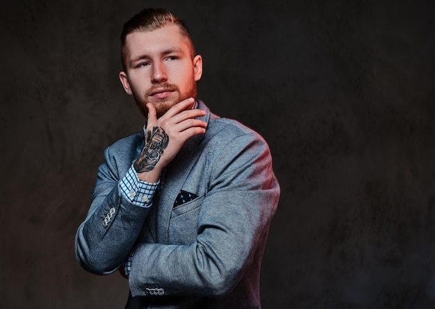 Studio portrait of redhead bearded male dressed in a suit posing over grey background.