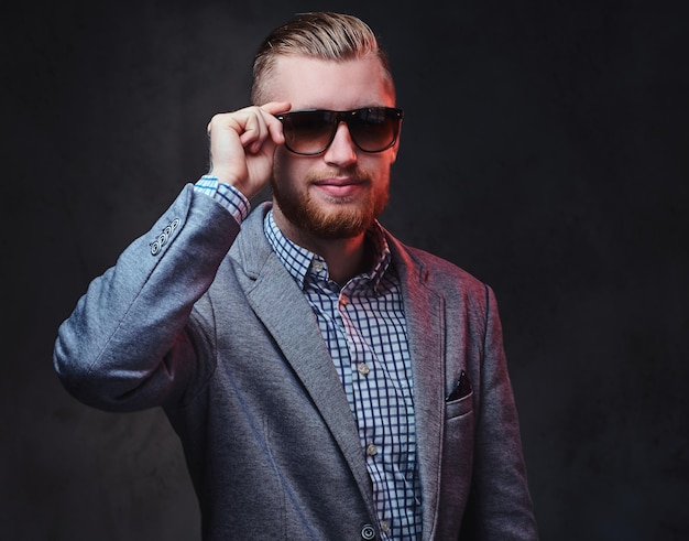 Free photo studio portrait of redhead bearded male dressed in a suit and sunglasses over grey background.