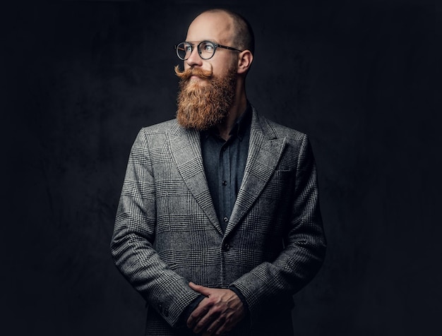 Studio portrait of redhead bearded male in vintage eyeglasses dressed in a wool jacket.