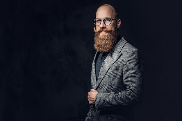 Studio portrait of redhead bearded male in vintage eyeglasses dressed in a wool jacket.