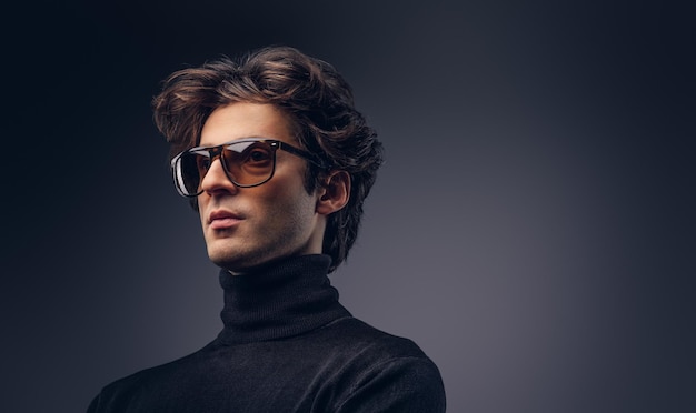 Студийный портрет чувственного мужчины-мачо со стильными волосами в черном свитере и солнечных очках.