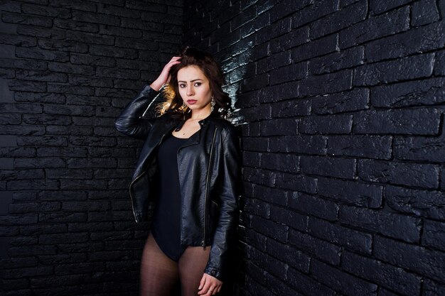 Studio portrait of sexy brunette girl in black leather jacket against brick wall