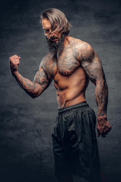 Free photo studio portrait of shirtless, tattooed bearded male over dark grey vignette background.