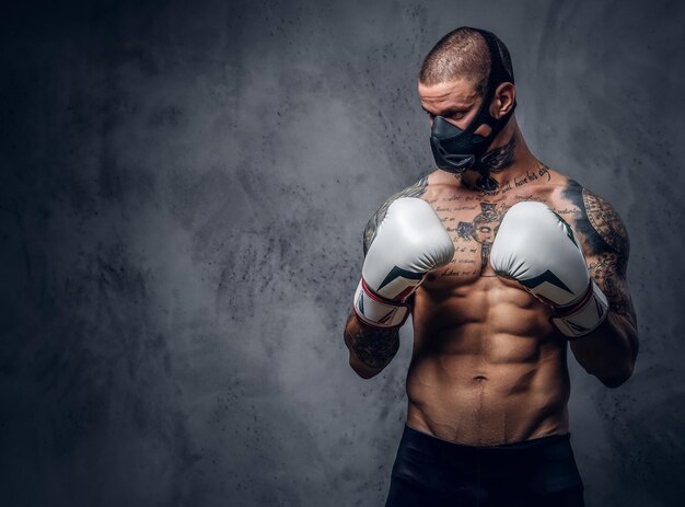 Studio portrait of shirtless, tattooed fighter male in a mask over grey vignette background.