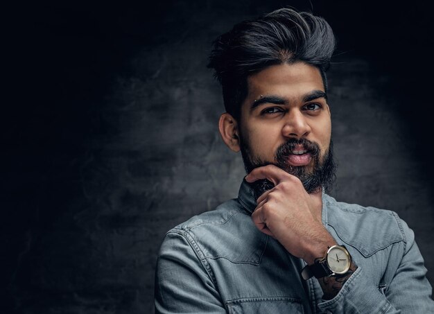 Studio portrait of stylish bearded Indian man in a blue shirt over grey background.