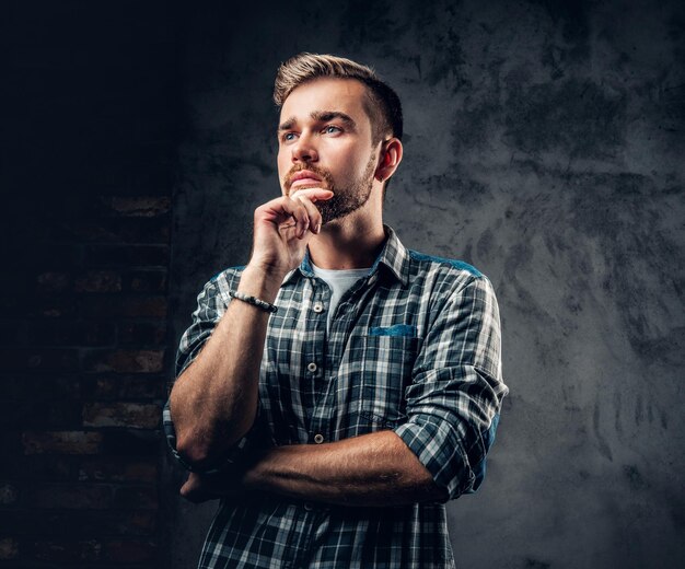 Studio portrait of thoughtful bearded hipster male over grey background.