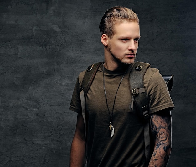 Studio portrait of urban style backpacker in Camo green t shirt and tattoos on arms.