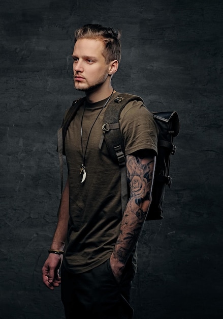 Free photo studio portrait of urban style backpacker in camo green t shirt and tattoos on arms.