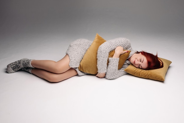 Studio portrait of a woman in a sweater hugging a pillow