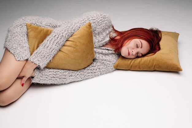 Студийный портрет женщины в свитере, обнимающей подушку
