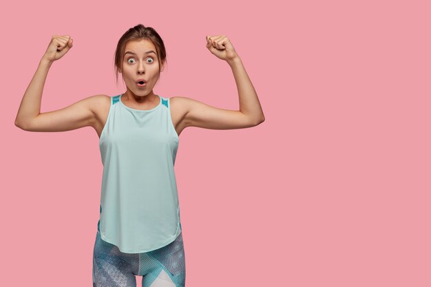 Studio shot of amazed woman shows biceps on both hands