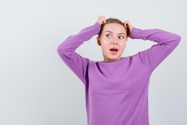 Studio shot of attractive blonde woman in purple sweater puts hand on head and dreams isolated on white background