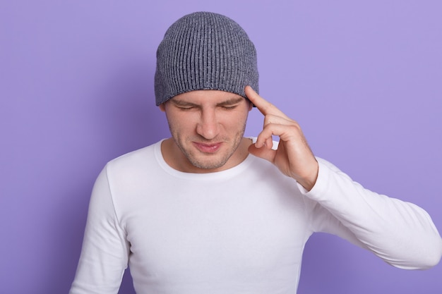 Studio shot of attractive male with closed eyes, keeps finger on temples, has terrible headache or forget something important