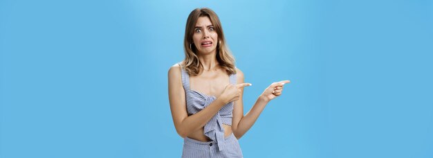 Studio shot of awkward displeased woman pointing left with index fingers making disgusted and