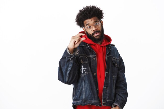 Studio shot of calm and chill goodlooking africanamerican male in glasses denim jacket over hoodie shaping small object as giving tiny hint telling put little more effort to achieve success