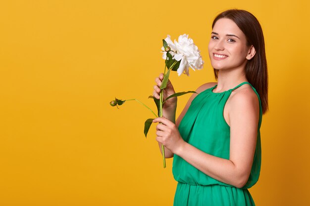 Studio shot of charming woman wearing elegant green sundress isolated over yellow