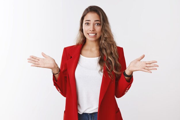 Studio shot clumsy silly cute female trainee apologizing saying oops smiling guilty awkward shrugging, put hands sideways sorry making mistake, explaining herself, standing white wall