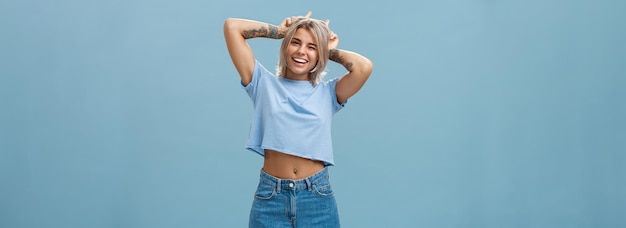 Free photo studio shot of cute attractive and joyful stylish blond woman with tattoos on arms winking and smili