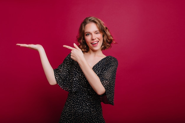 Studio shot of cute young lady playfully posing on bright background and winks