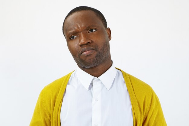 Studio shot of displeased dissatisfied young Afro American male dressed in yellow cardigan and white shirt frowning, feeling offended and disappointed. Human emotions, feelings and reaction