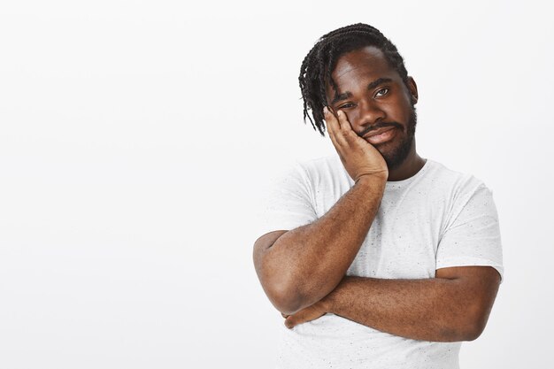 Studio shot of displeased guy with braids posing against the white wall