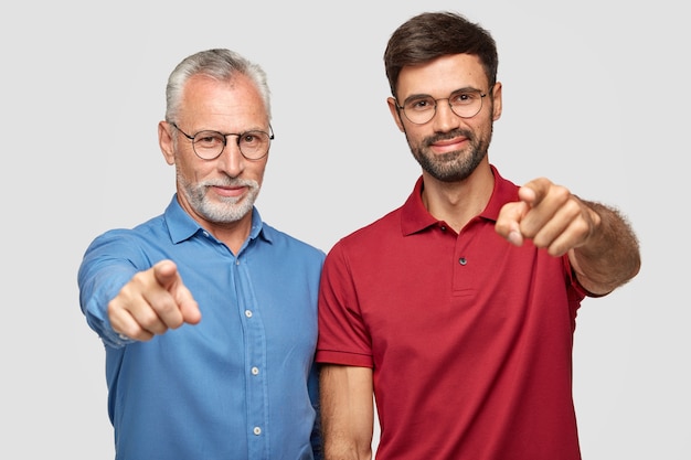 Studio shot of elderly man and bearded male adult stand next to each other indoor