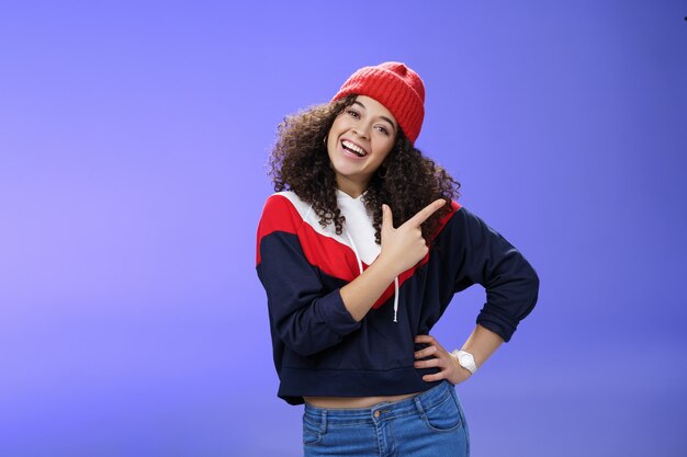 Studio shot of enthusiastic charming curlyhaired woman inviting to play in snow with her pointing at.