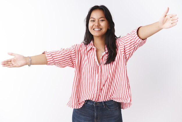 Studio shot of friendly  asian girl extending hands sideways wide and  smiling