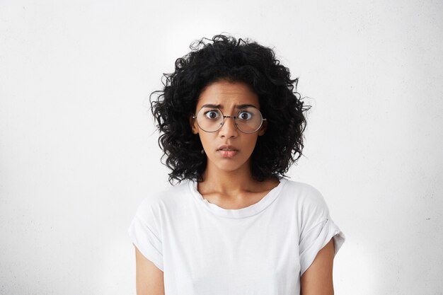 Studio shot of frightened bug-eyed young female feeling scared and shocked