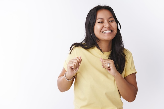 Studio shot of funny and enthusiastic upbeat joyful female in yellow t-shirt making dance moves shaking body and hands attending awesome party with cool music over white background