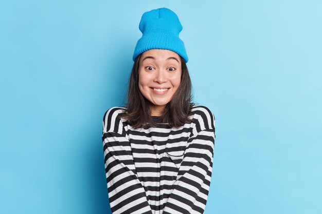 Studio shot of glad pretty Asian woman with dark hair looks happily