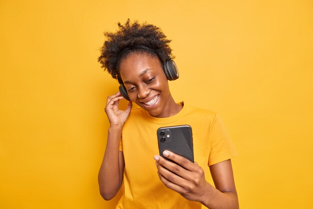 Studio shot of good looking dark skinned woman enjoys favorite playlist listens to  music via headphones