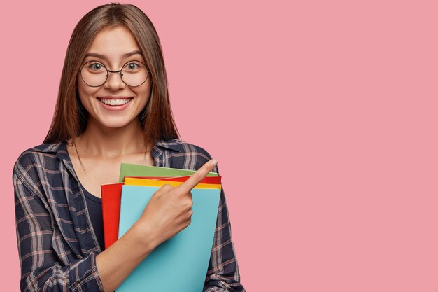 Studio shot of good looking young businesswoman posing against the pink wall with glasses