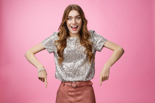 Studio shot impressed excited attractive young fashionable woman drop jaw thrilled pointing down ind...