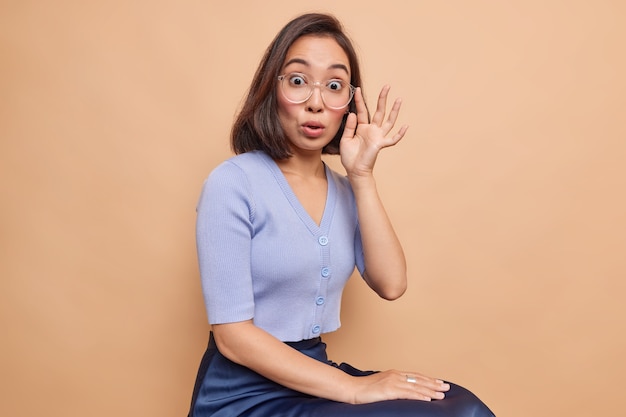 Studio shot of impressed young Asian woman with dark hair stares impressed