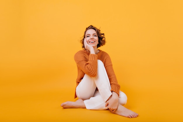 Studio shot of laughing gorgeous woman posing with legs crossed